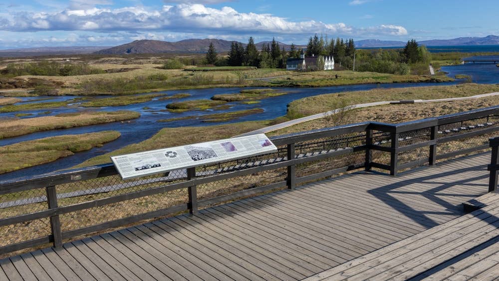 Boardwalk through Almannagjá with Þingvellir church and the Öxará river beyond.