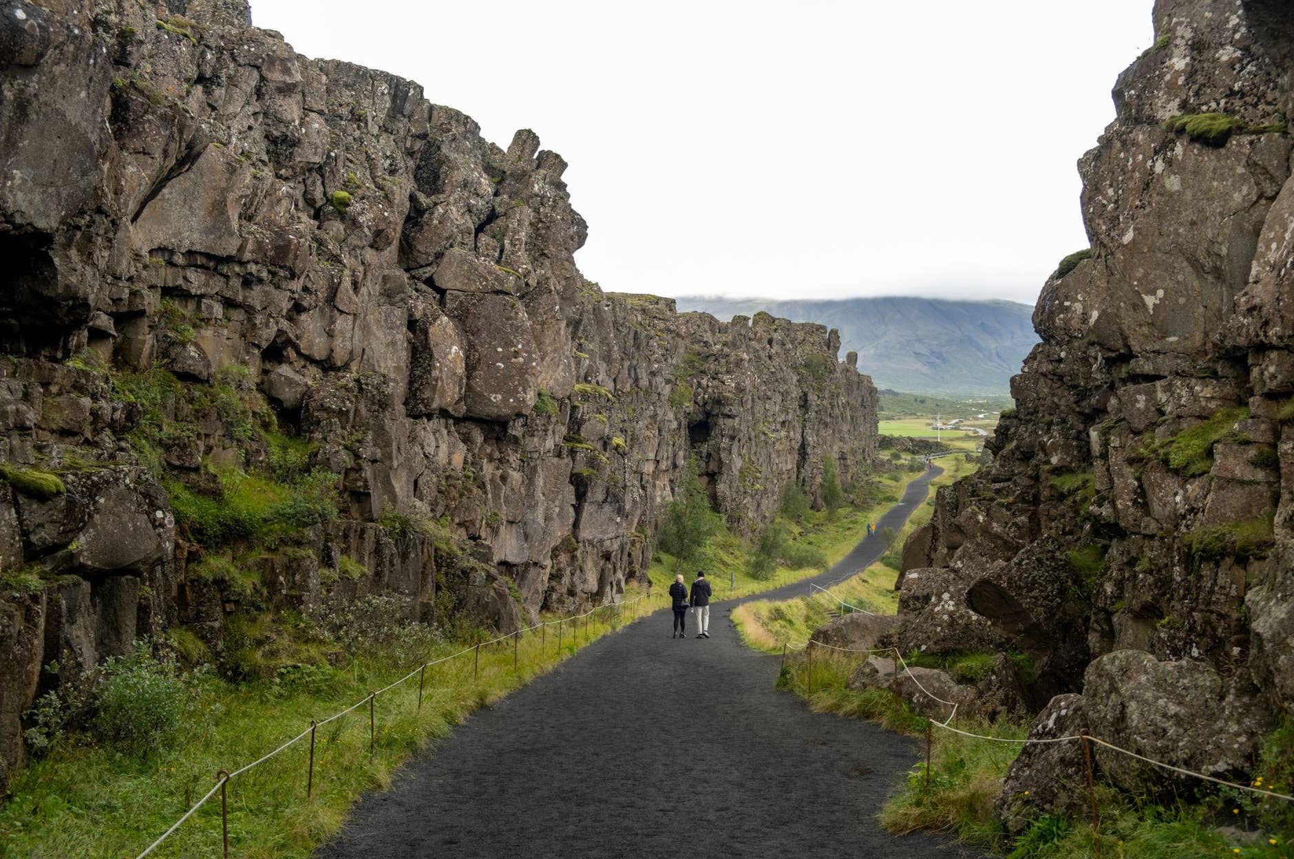 People walking below mossy volcanic cliffs on the Almannagjá path.