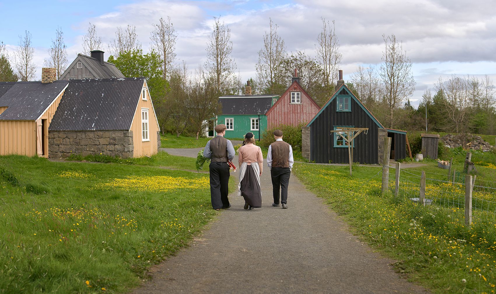 Costumed interpreters walking between colorful historic buildings at Árbær Open Air Museum.