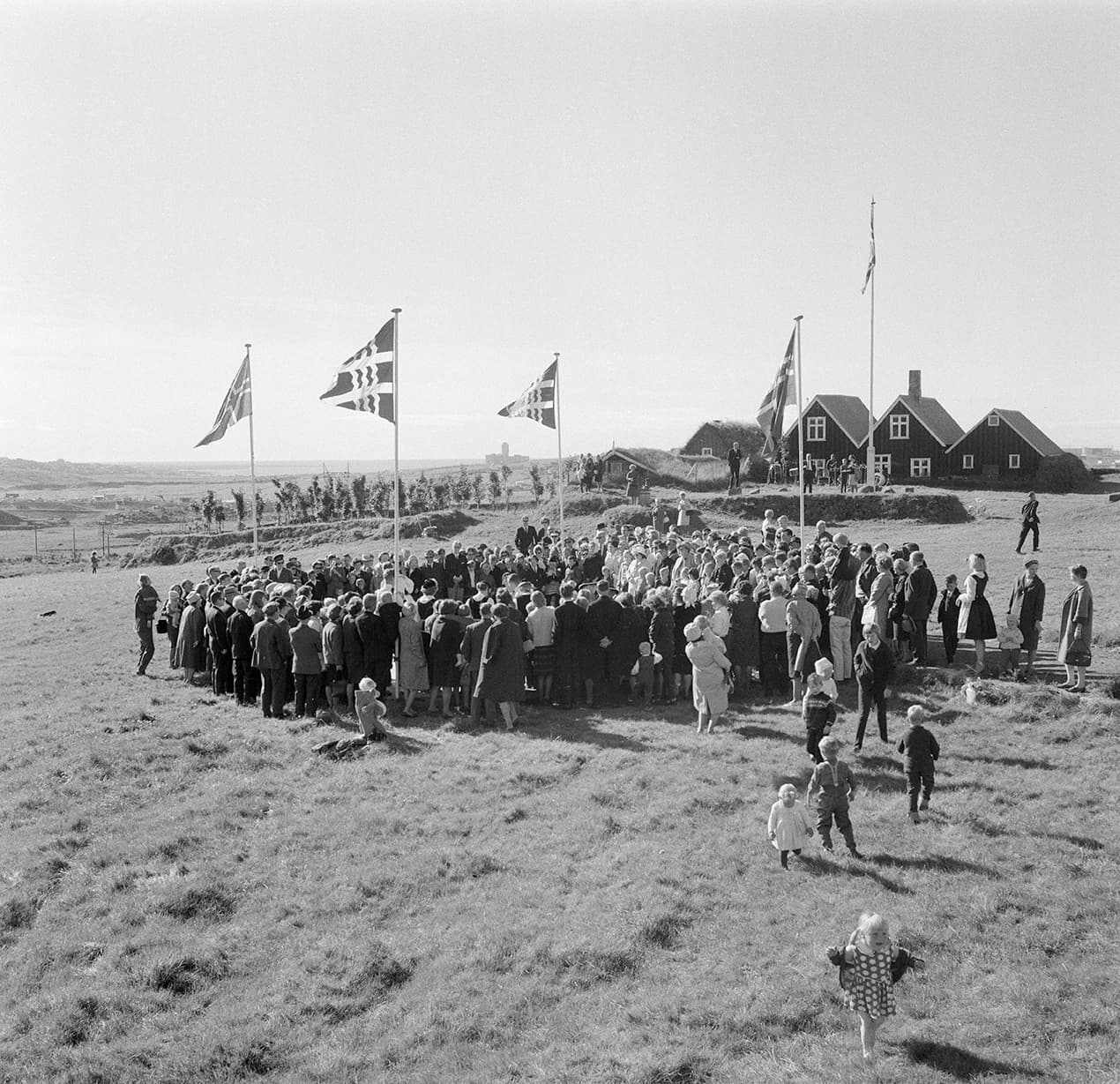 Historic black-and-white scene of a crowd at Árbæjarsafn with turf buildings in the background.