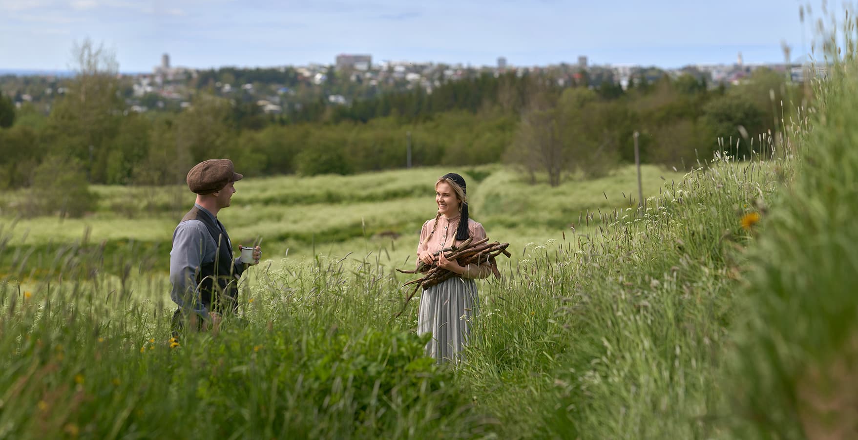 Costumed museum interpreters in the grassy Árbæjarsafn landscape with Reykjavík in the distance.