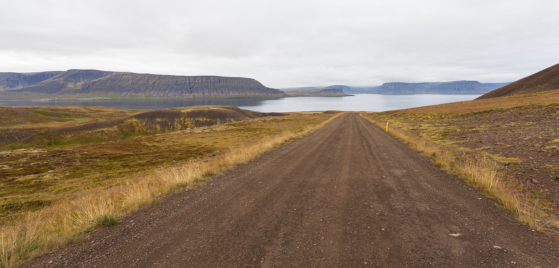 Gravel road descending toward Arnarfjörður with flat-topped Westfjords mountains across the water.
