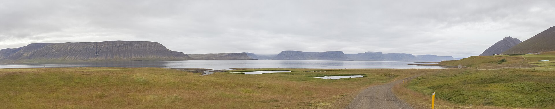 Wide Arnarfjörður panorama with low clouds, a rough road, small ponds, and mountains around the fjord.