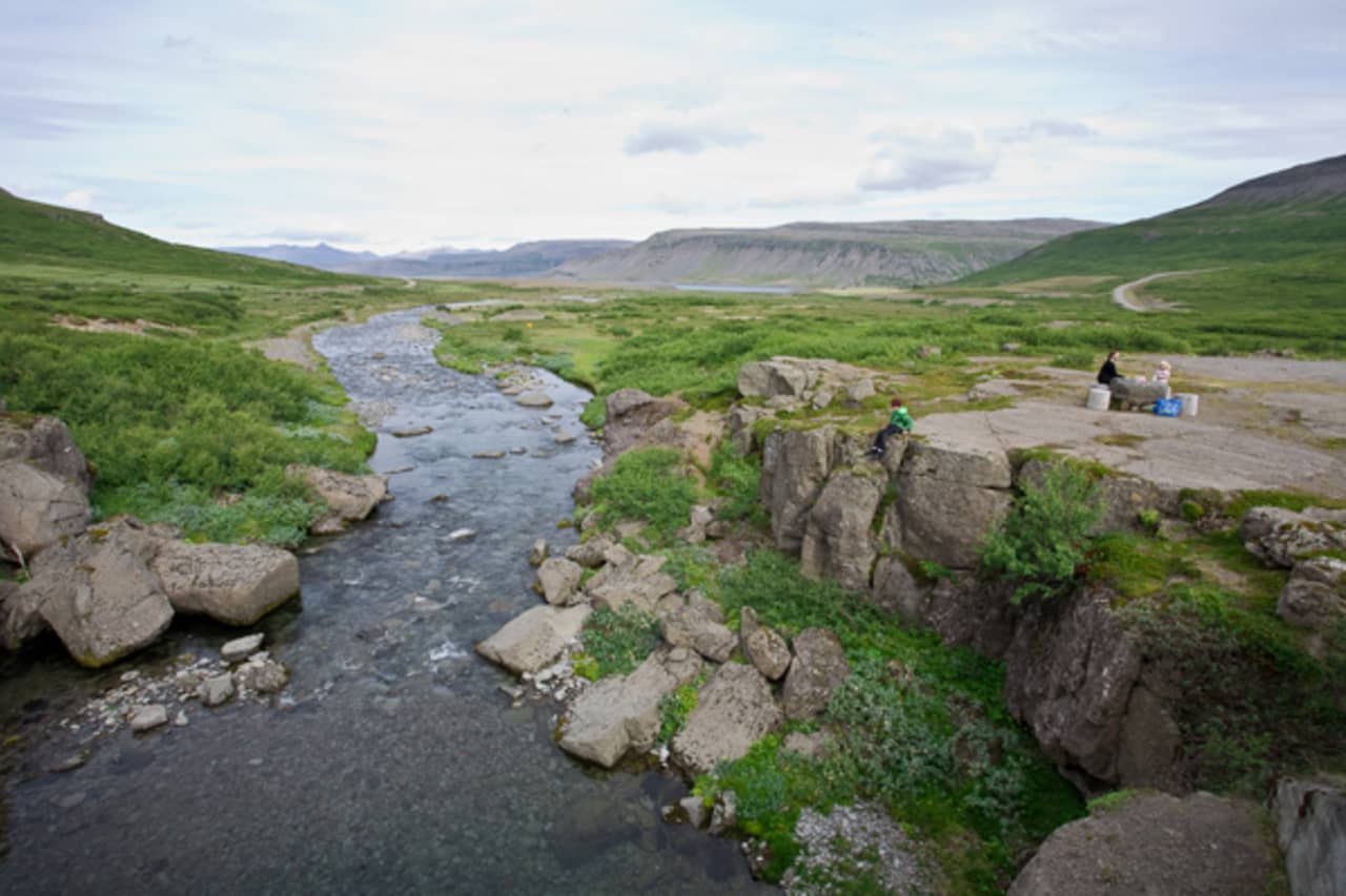 Rocky stream, roadside area, and people beside Trostansfjörður in the Arnarfjörður fjord system.