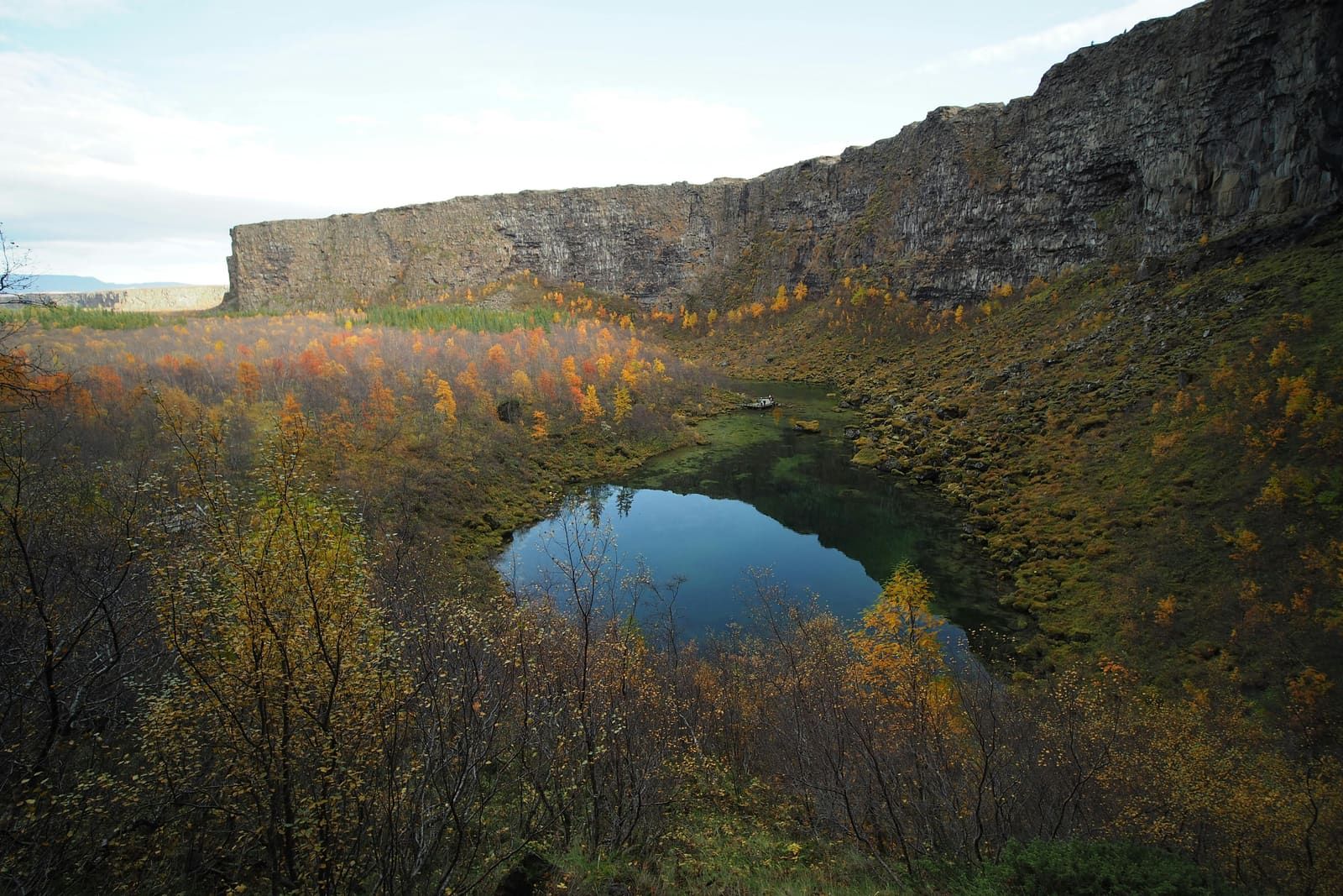 Botnstjörn pond at Ásbyrgi surrounded by autumn birch and cliff walls.