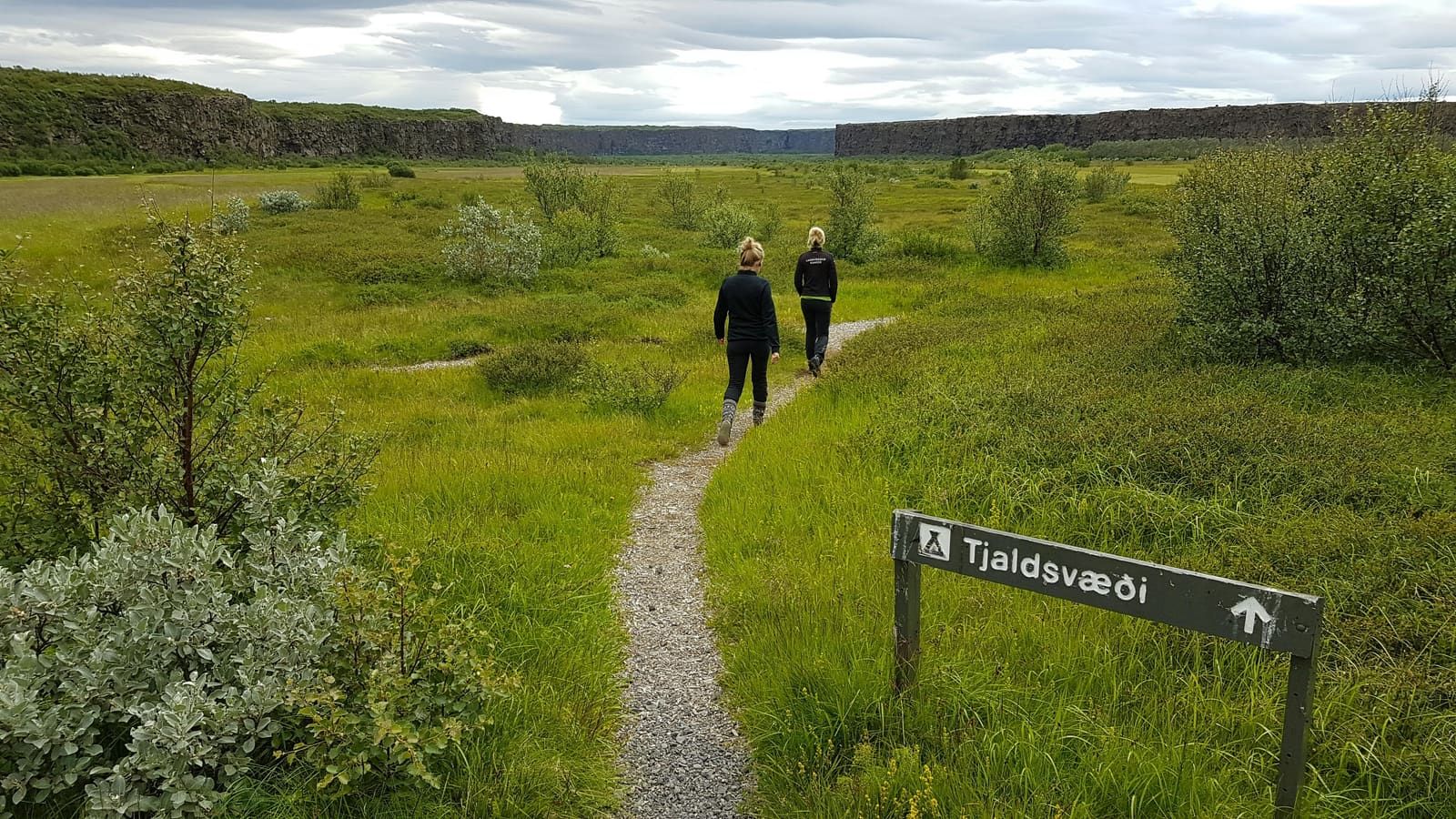 Walkers on a broad path near Gljúfrastofa with Ásbyrgi canyon walls in the distance.