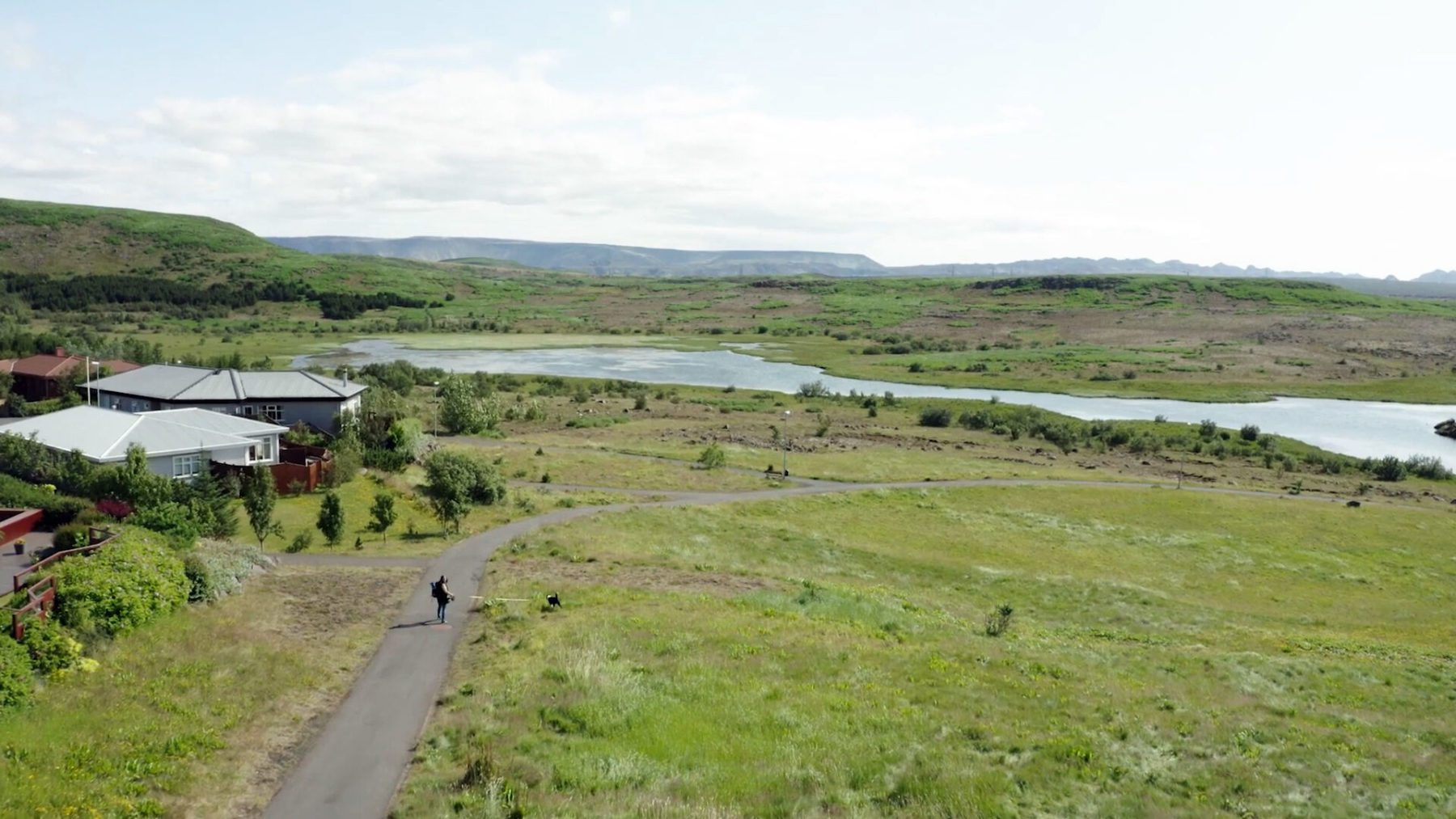 Ástjörn Lake footpath in Hafnarfjörður with green shoreline and calm water.