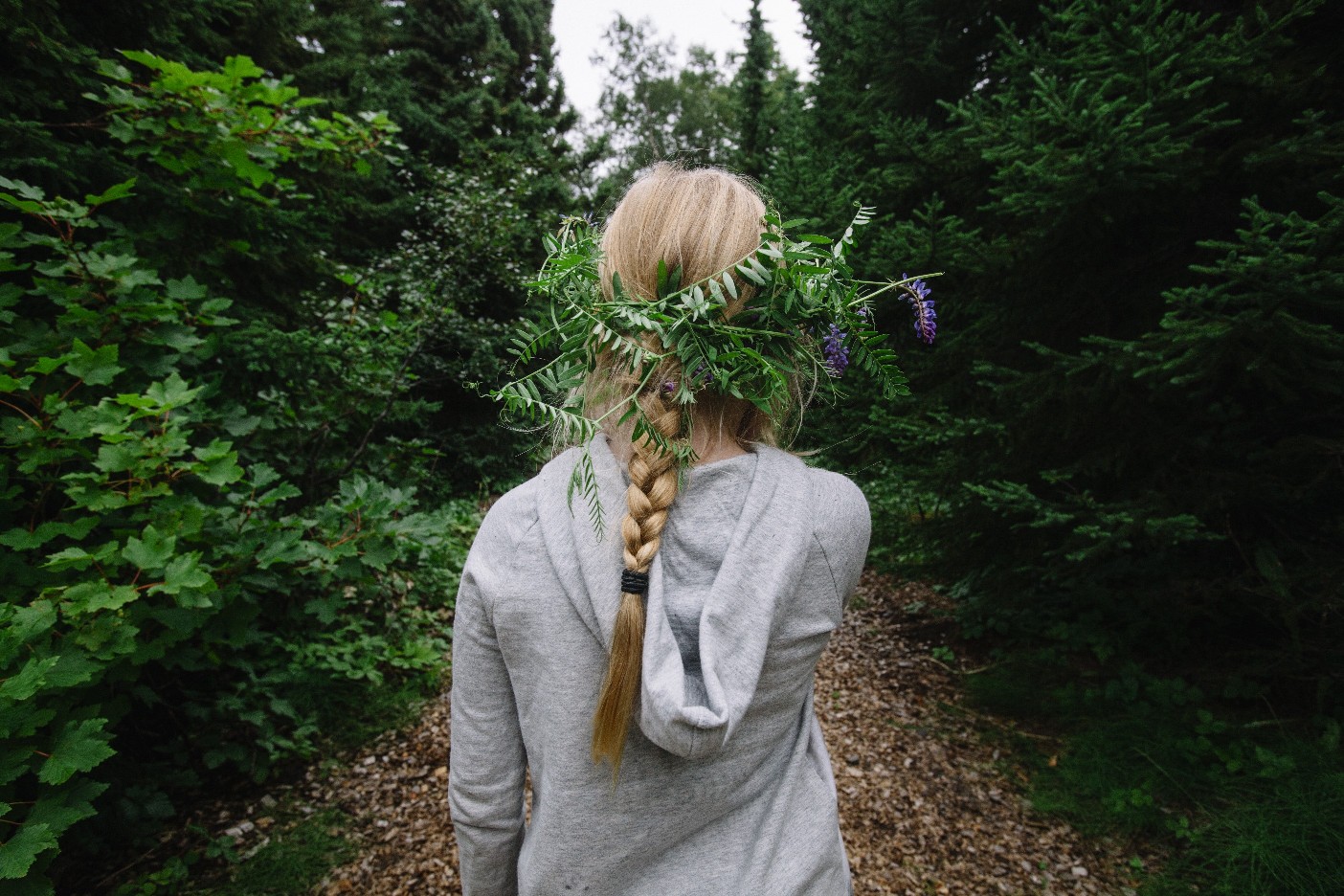 A person walking through dense Hallormsstaður forest on a narrow path near Atlavík and Lake Lagarfljót.