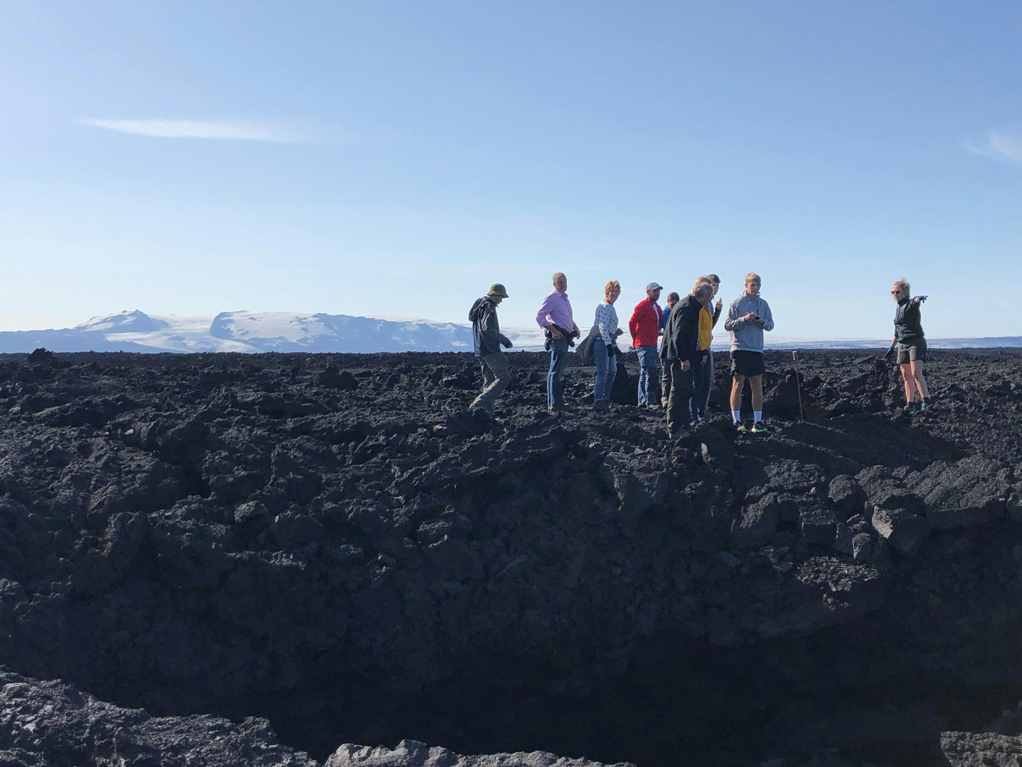 Visitors standing on the dark Holuhraun lava field with Vatnajökull in the distance.