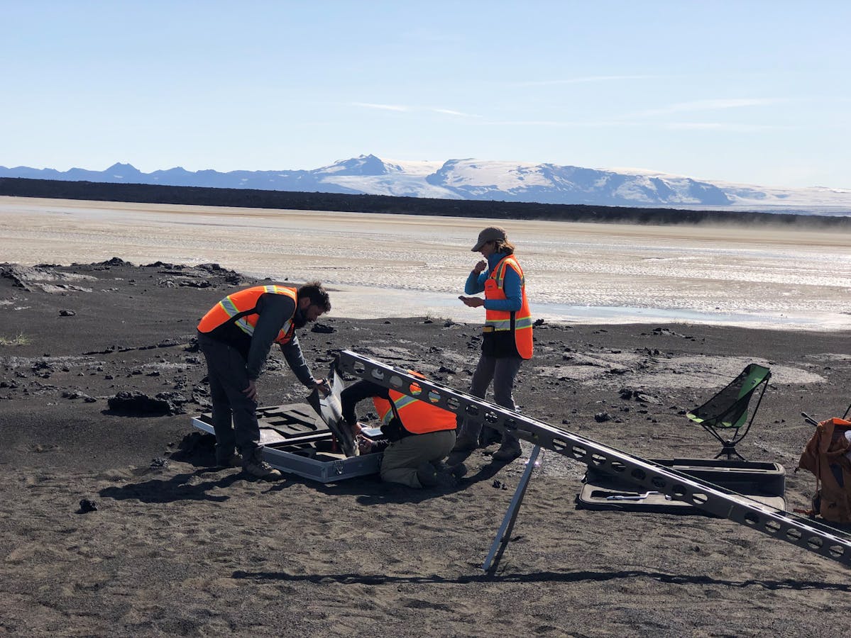 Researchers working on black sand and lava near Holuhraun with Vatnajökull visible in the distance.