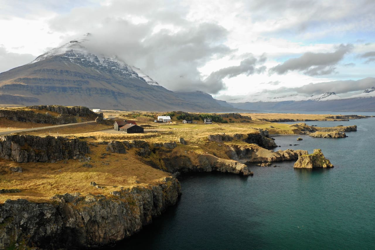 Teigarhorn coastline and dark cliffs on Berufjörður with farm buildings and Búlandstindur across the fjord.