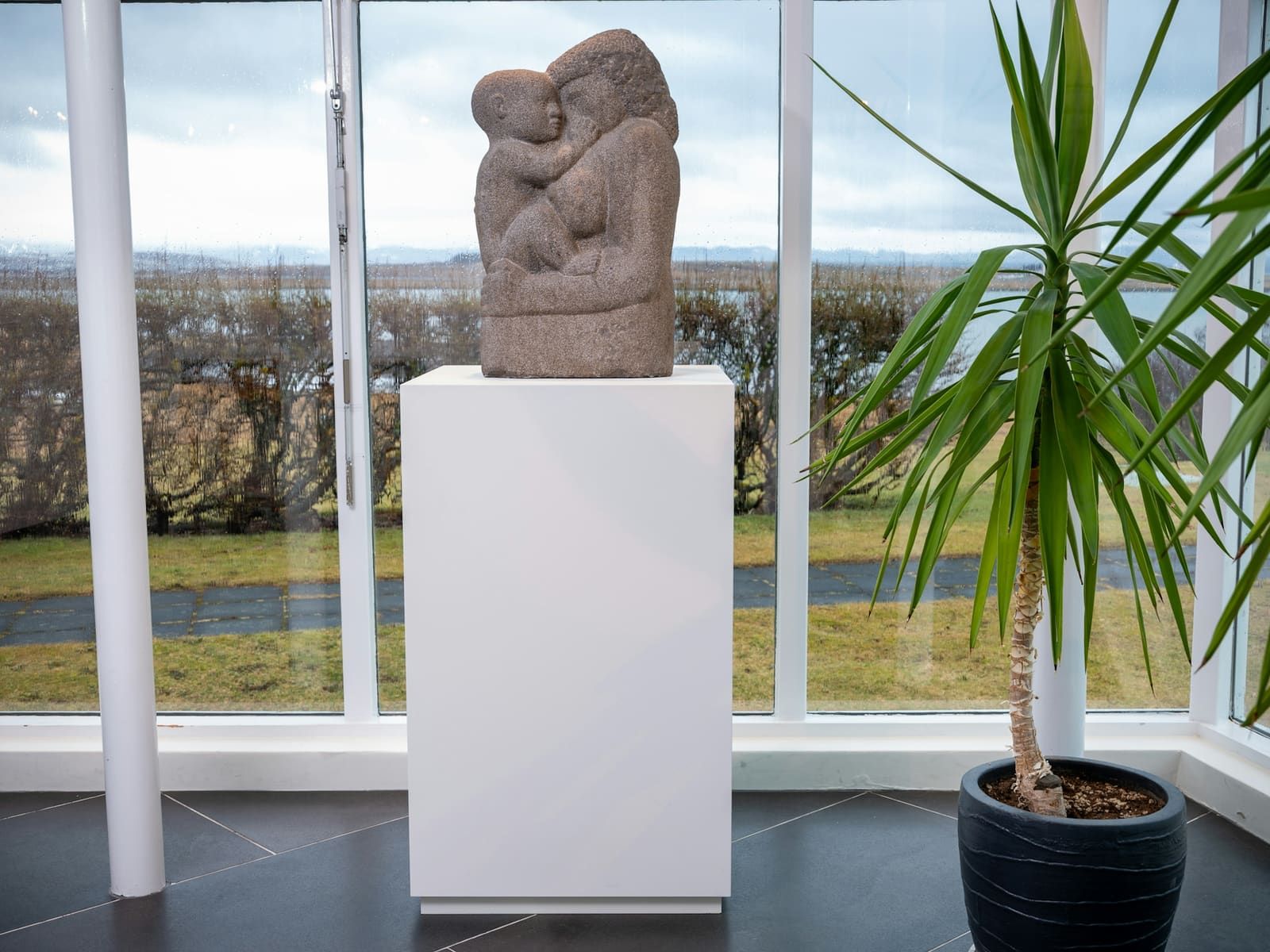 Stone sculpture displayed by a window inside Bessastaðir with Álftanes landscape outside.