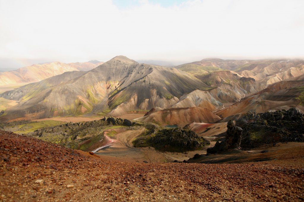Reddish gravel on Bláhnjúkur with grey and striped Landmannalaugar mountains beyond the trail.