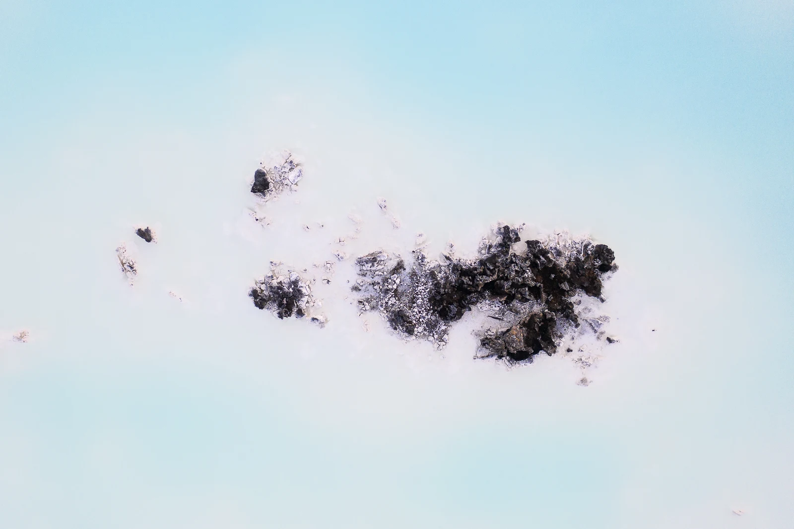 Aerial view of pale Blue Lagoon geothermal water surrounding black lava rocks.