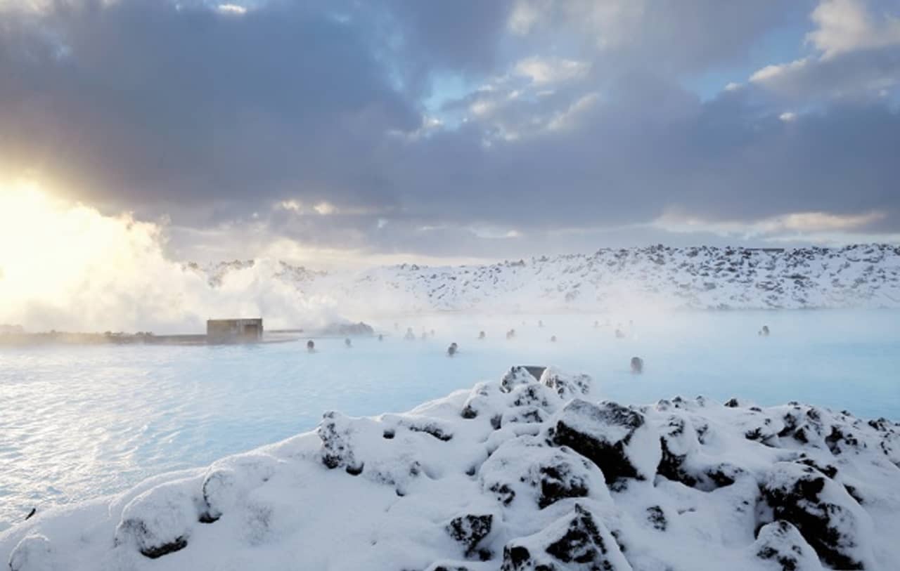 Steam rising from the Blue Lagoon on a snowy winter day with bathers in the pale water.