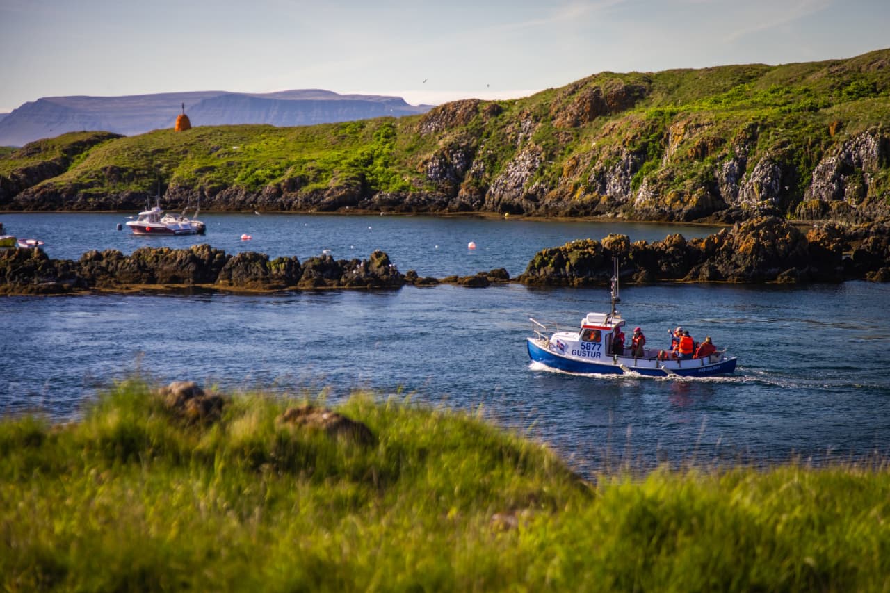 Small boat crossing the harbor water beside low cliffs on Flatey island.