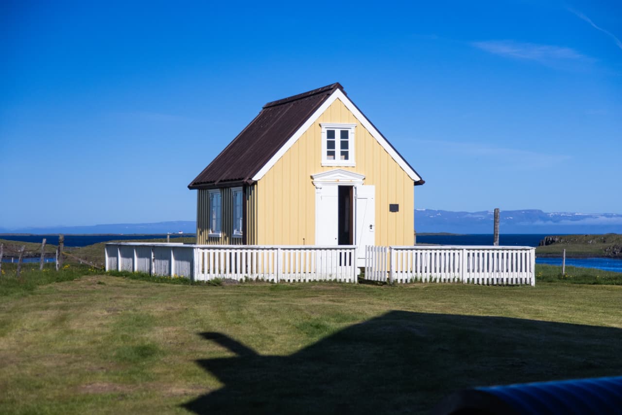 Small yellow church on Flatey island with Breiðafjörður water beyond the fence.