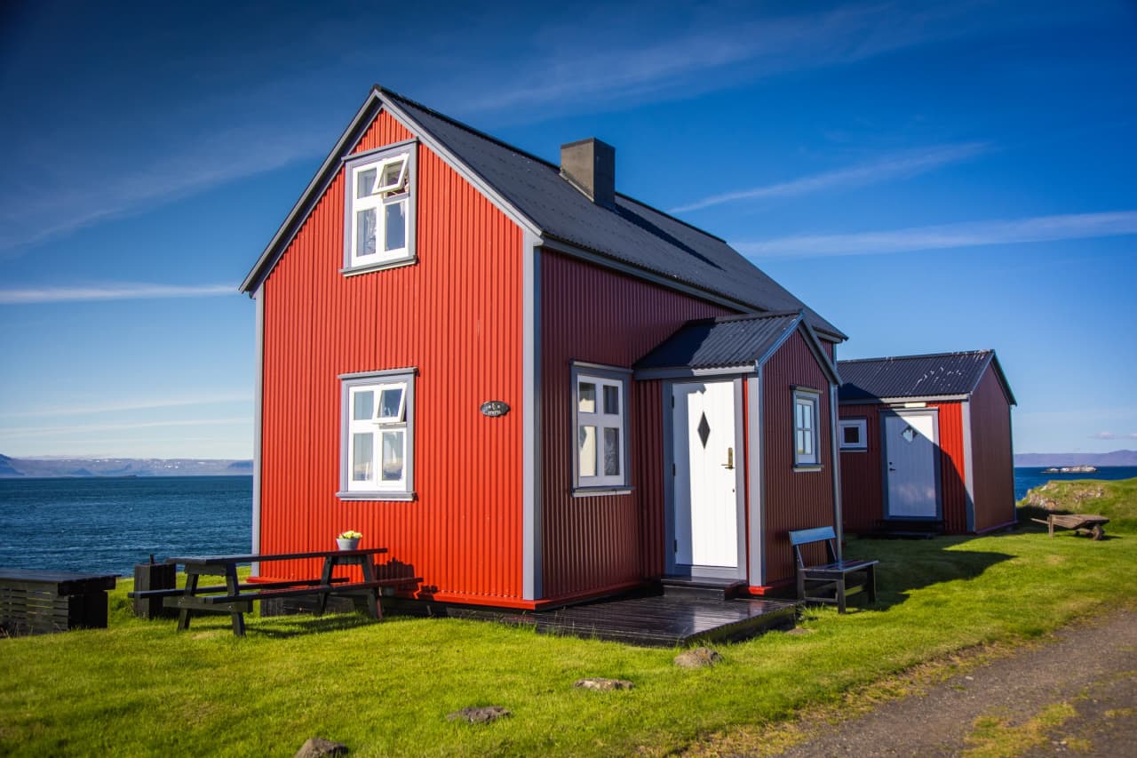 Red timber house on Flatey island with grass paths and Breiðafjörður water nearby.