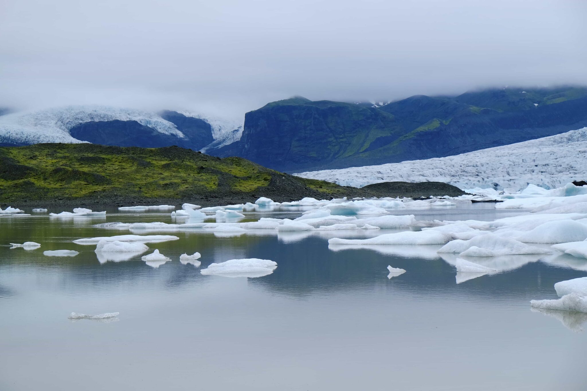 Icebergs floating on Breiðárlón Glacier Lagoon below dark mountains and Vatnajökull ice.