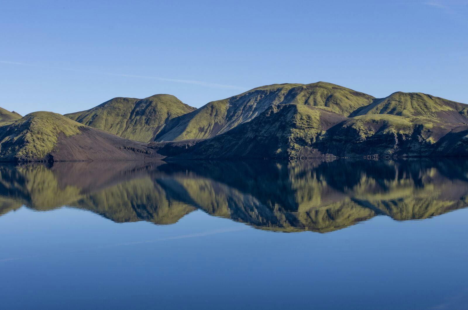 Mossy Fögrufjöll mountains reflected in calm Langisjór water near the Breiðbakur highland area.