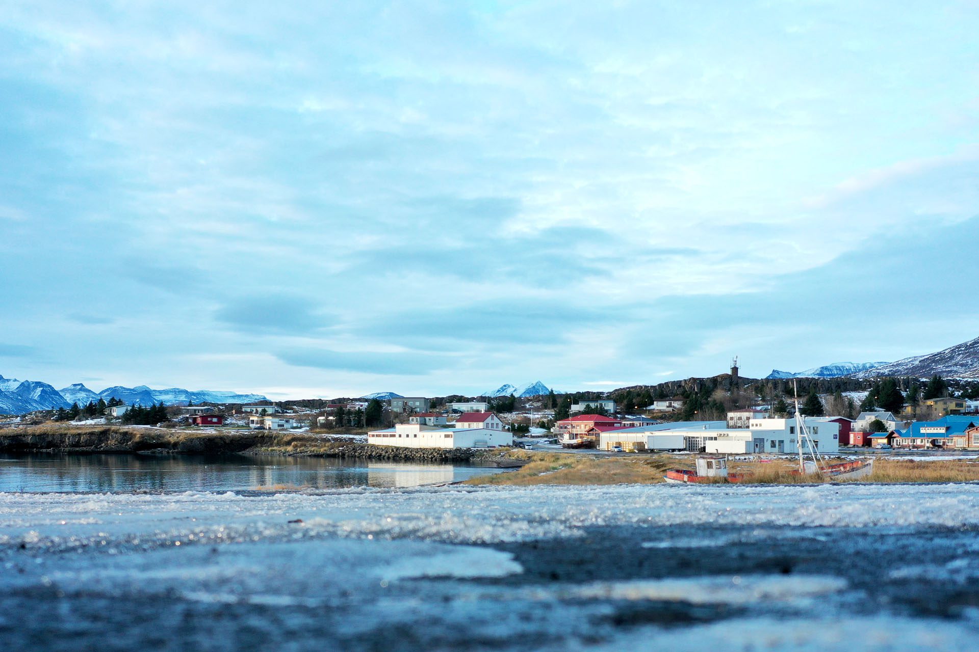 Breiðdalsvík village beside the bay with low buildings, mountains, and snow-edged shoreline in East Iceland.