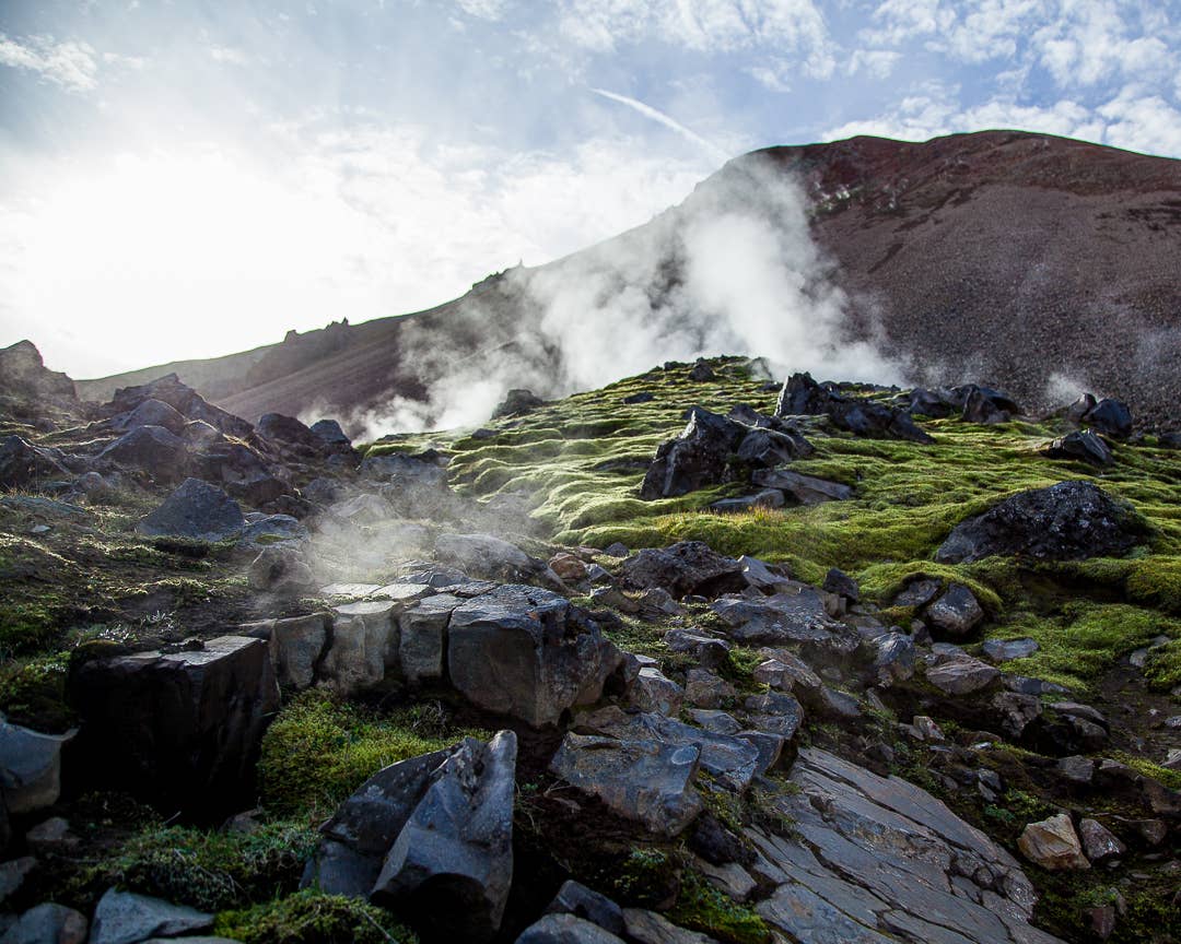 Geothermal steam rising from mossy rocks below dark slopes near Brennisteinsalda in Landmannalaugar.