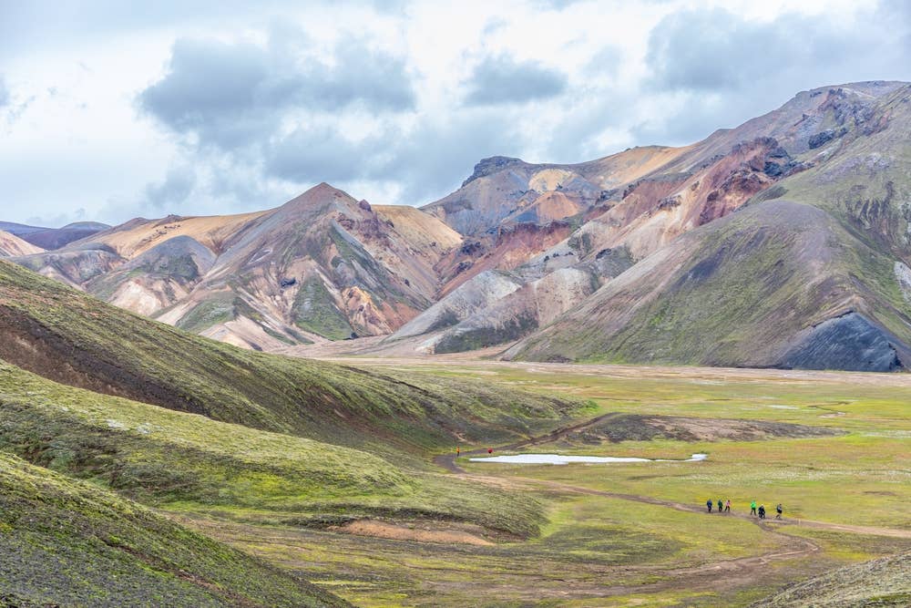 Hikers on a trail below colorful rhyolite slopes near Brennisteinsalda in Landmannalaugar.