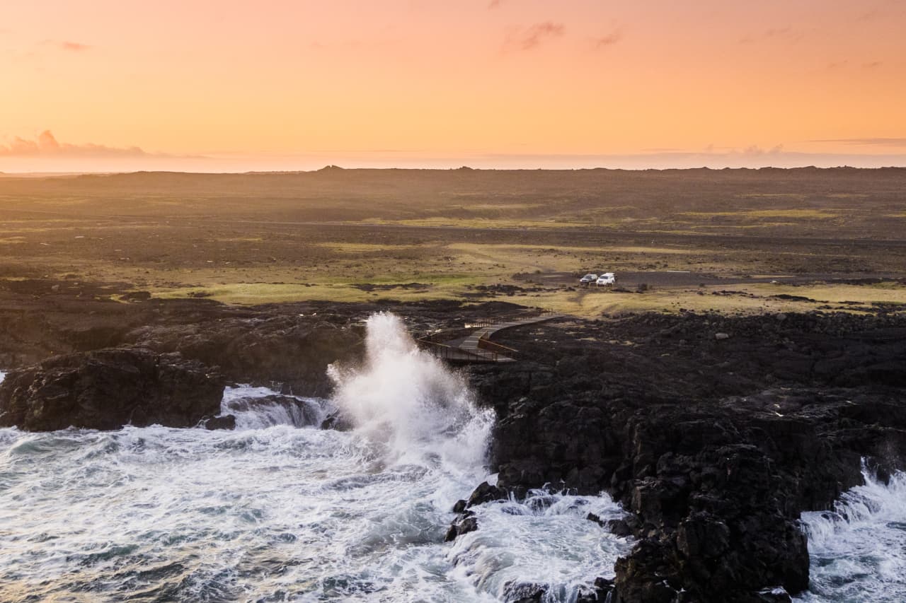 Sunset light over Brimketill as waves strike the black lava shore below the viewing platform.