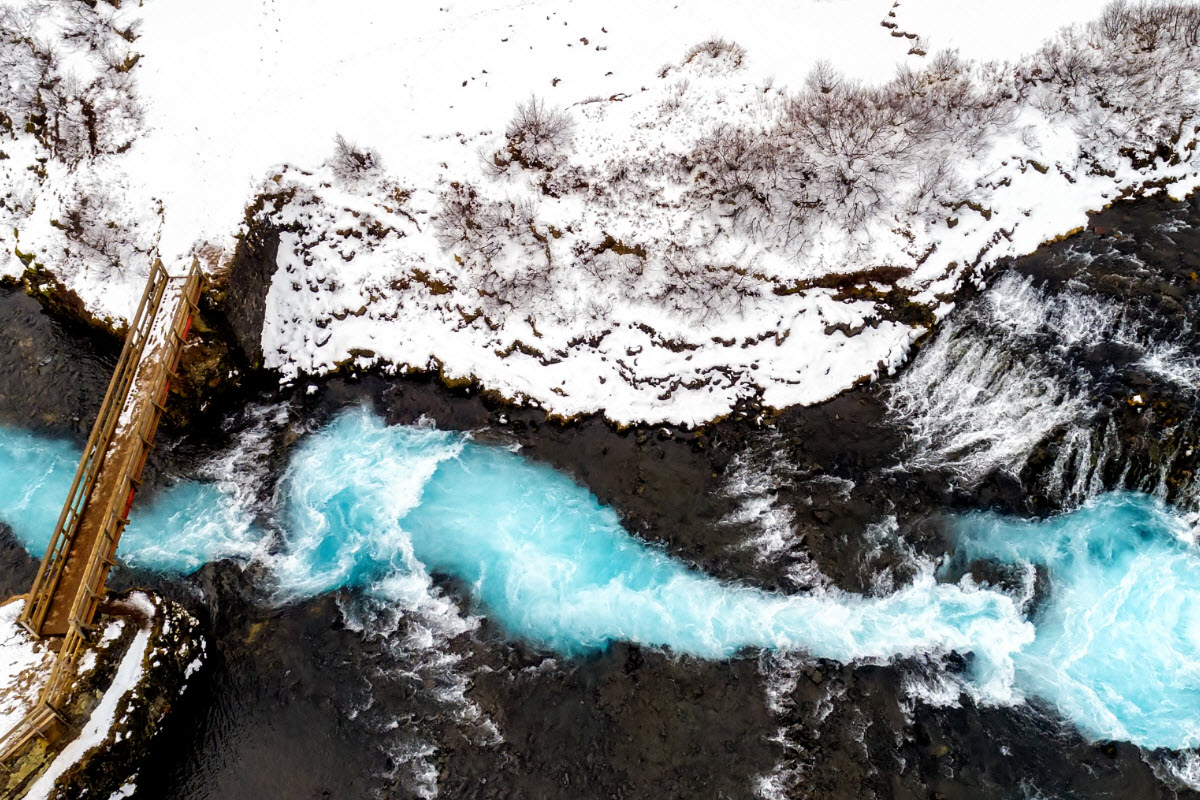 Overhead view of the blue Brúará channel and bridge near Brúarfoss in winter.