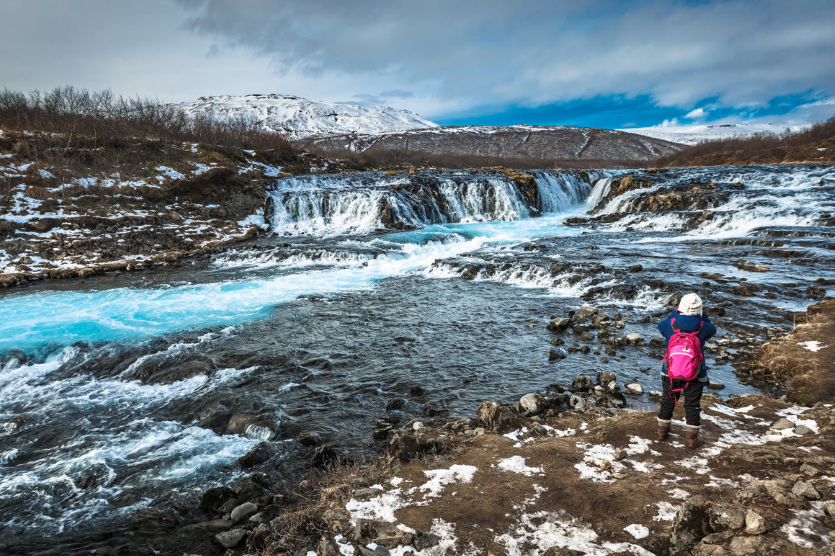 Visitor standing near Brúará and Brúarfoss with snow around the blue river.