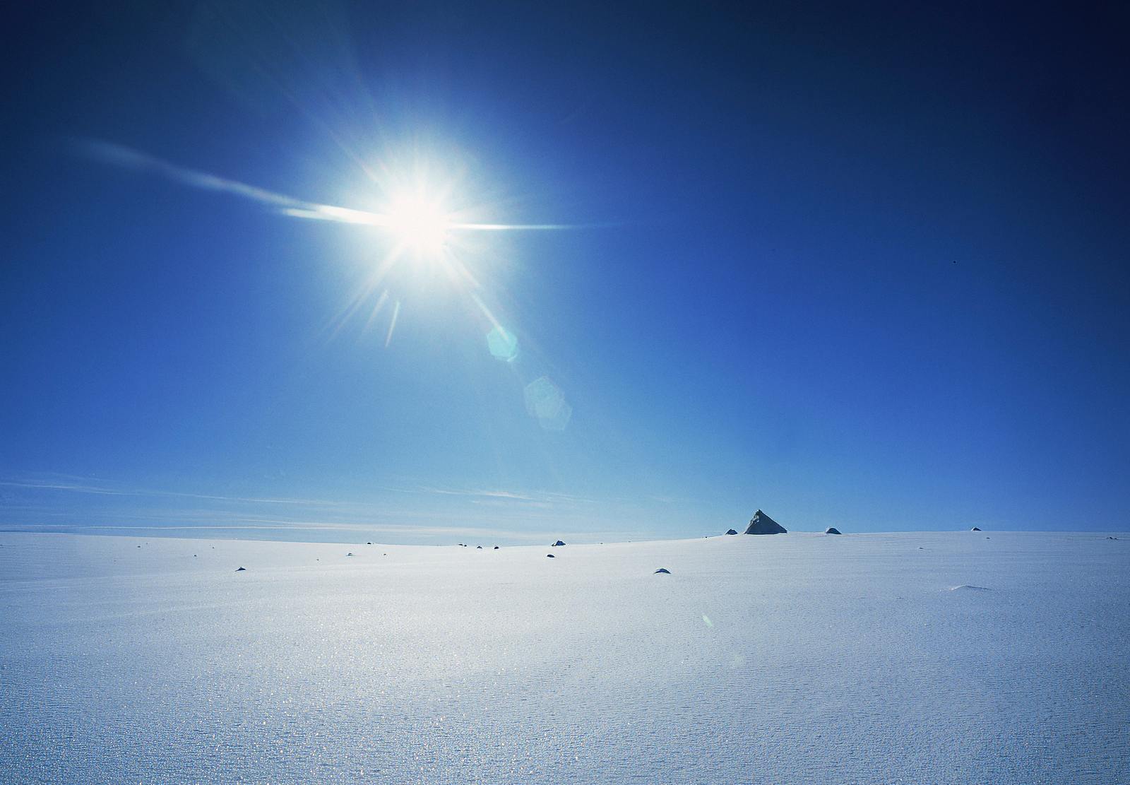 Bright snow and small dark nunatak peaks across the Brúarjökull icefield under a clear blue sky.