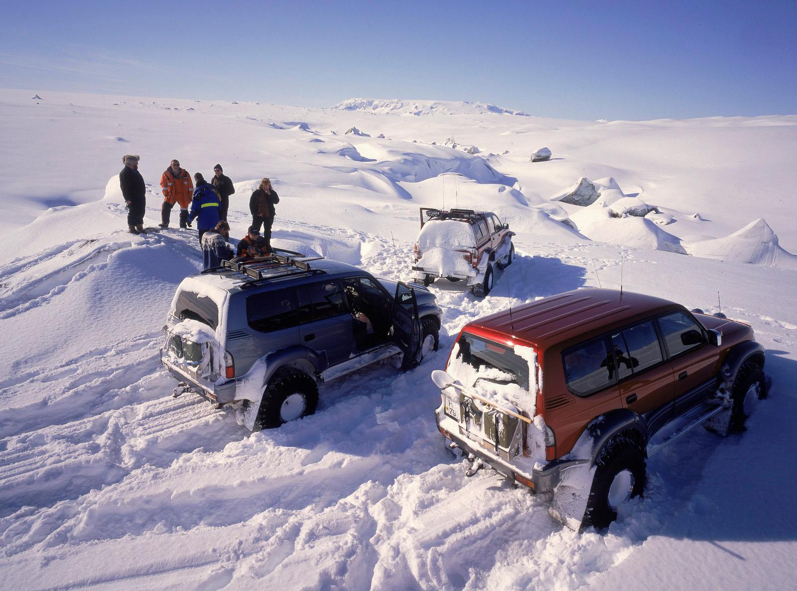 Super jeeps and travelers parked on deep snow beside the Brúarjökull glacier landscape.
