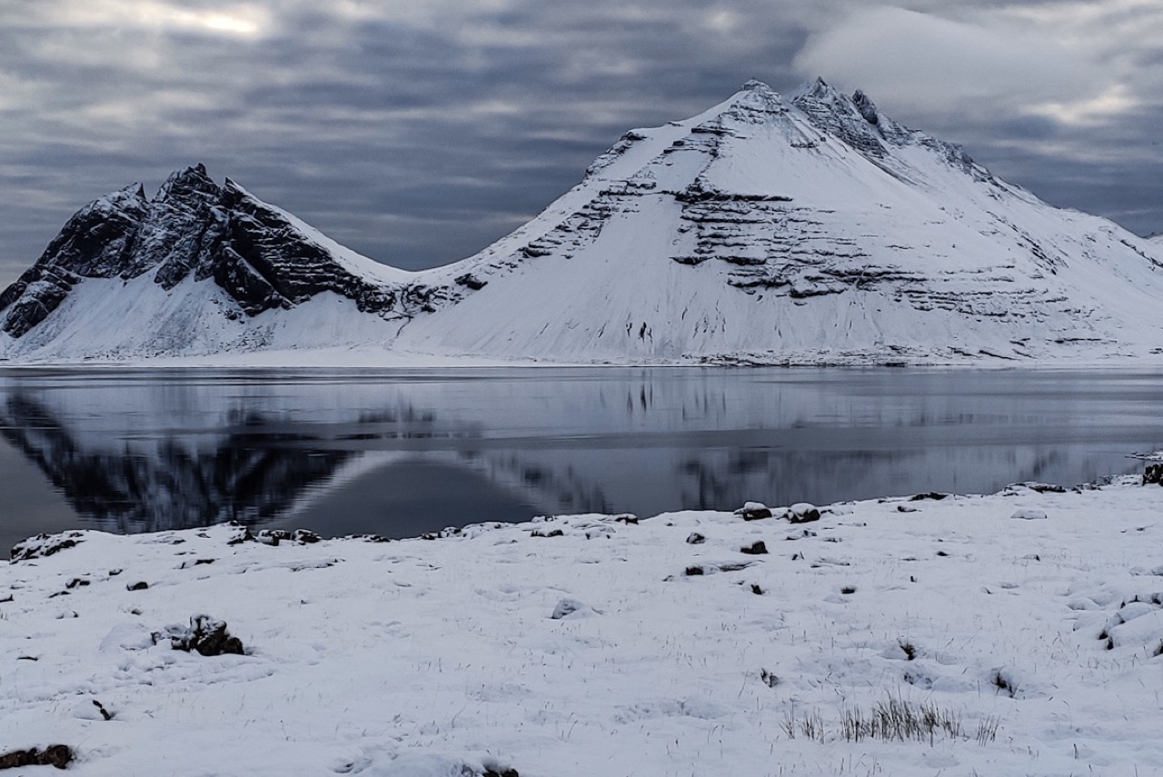 Snowy Brunnhorn reflected in calm water under a dark winter sky near Höfn.
