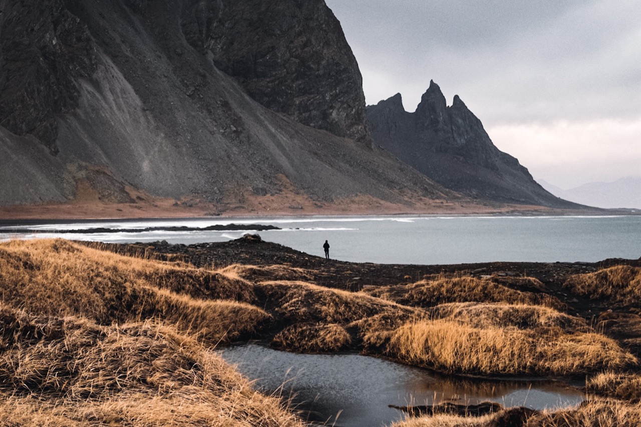 Brunnhorn's pointed Batman-like peaks above coastal water and rough grass near Höfn.