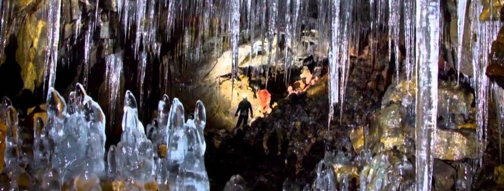 A wide view of icicles, ice mounds, and a small headlamp-lit figure inside Búri Lava Cave.