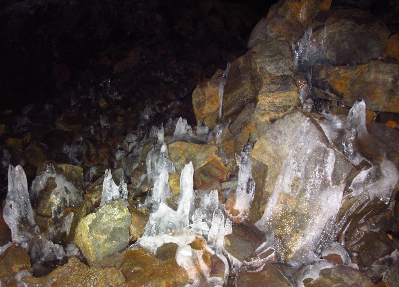 Clear ice formations rising from a rocky floor inside Búri Lava Cave.