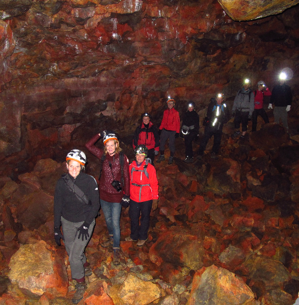Helmeted visitors standing on uneven red and black lava rocks inside Búri Lava Cave.