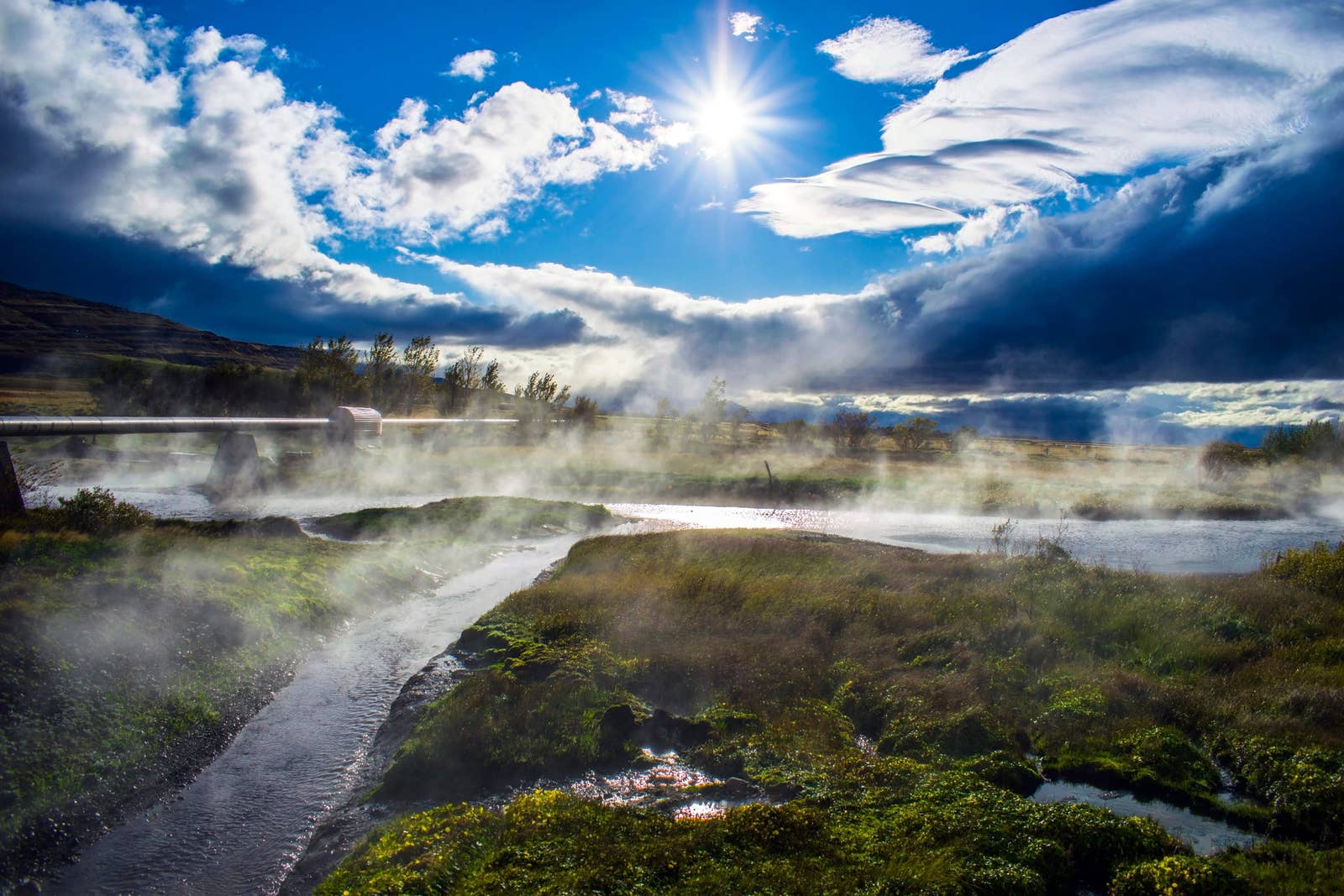 Steam rising over hot water channels and grassy ground at Deildartunguhver in West Iceland.