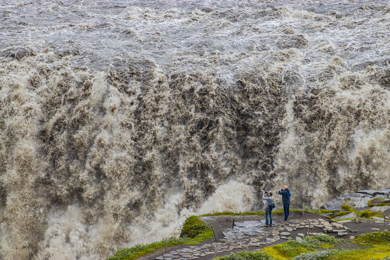 Visitors standing near the Dettifoss viewpoint beside the roaring glacial water.