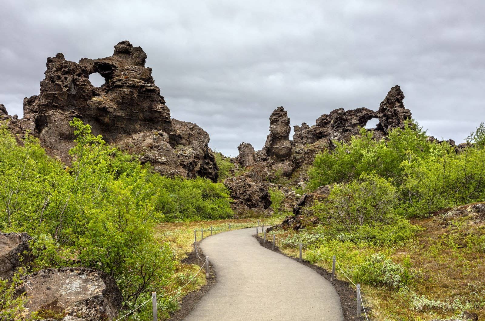 Marked walking path winding between dark Dimmuborgir lava towers and green summer birch.