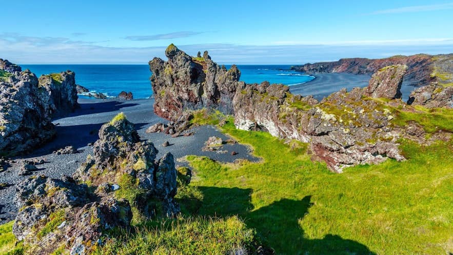 Lava formations above Djúpalónssandur with the black beach and blue Atlantic water beyond.