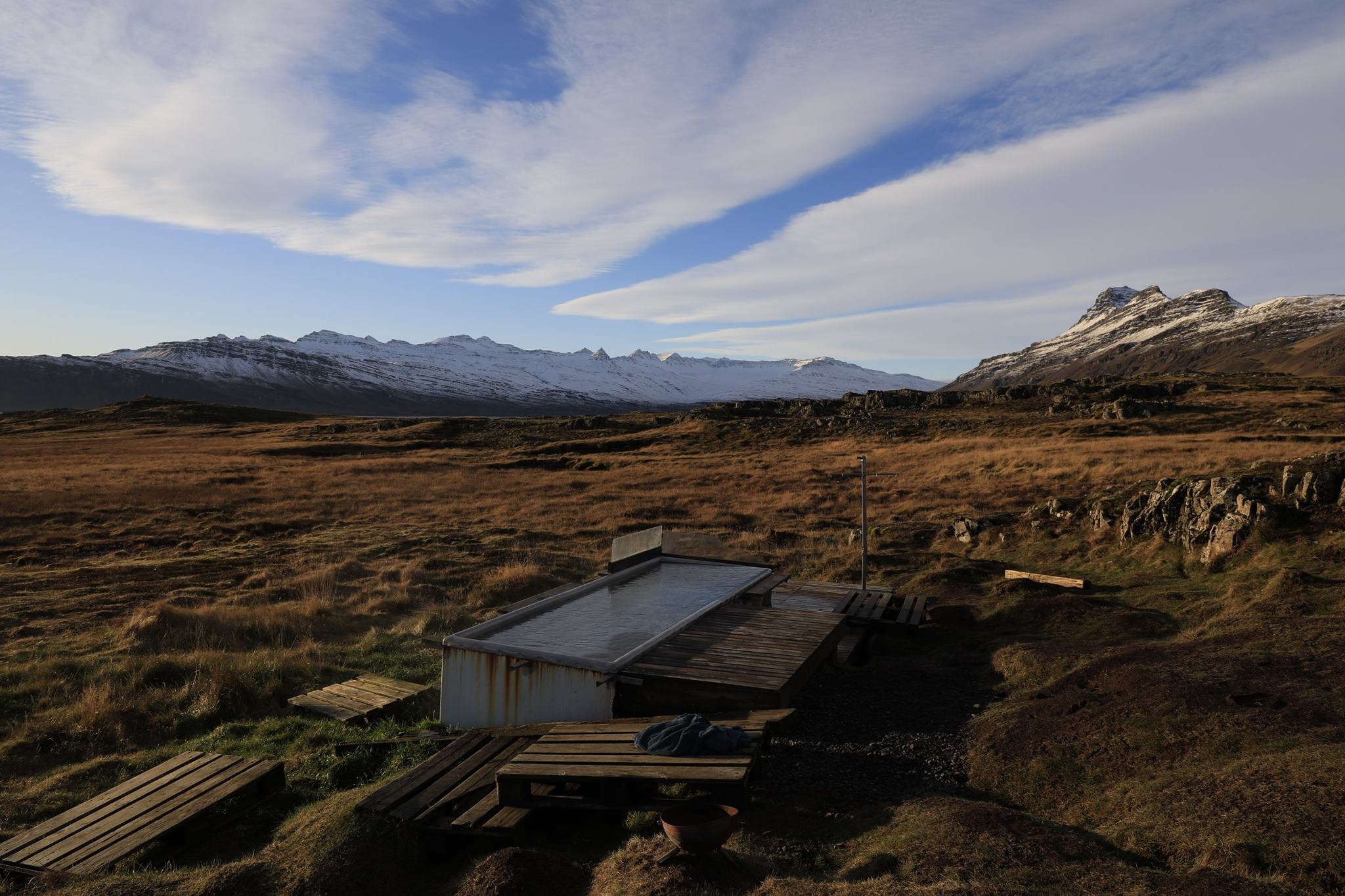Wide view of Djúpavogskörin hot spring below rocks with open East Iceland mountains beyond.