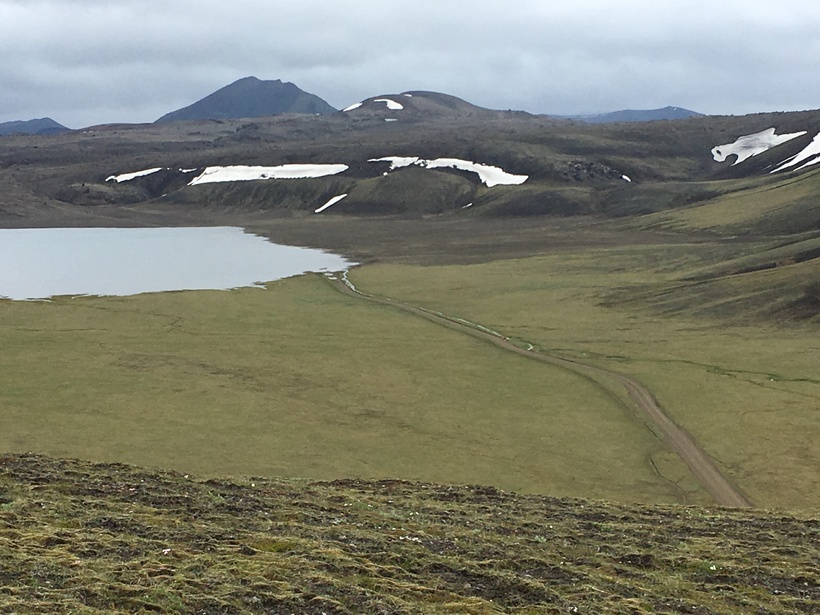 Dómadalsvatn lake and a rough track across the green Dómadalur valley floor below dark Highland hills.