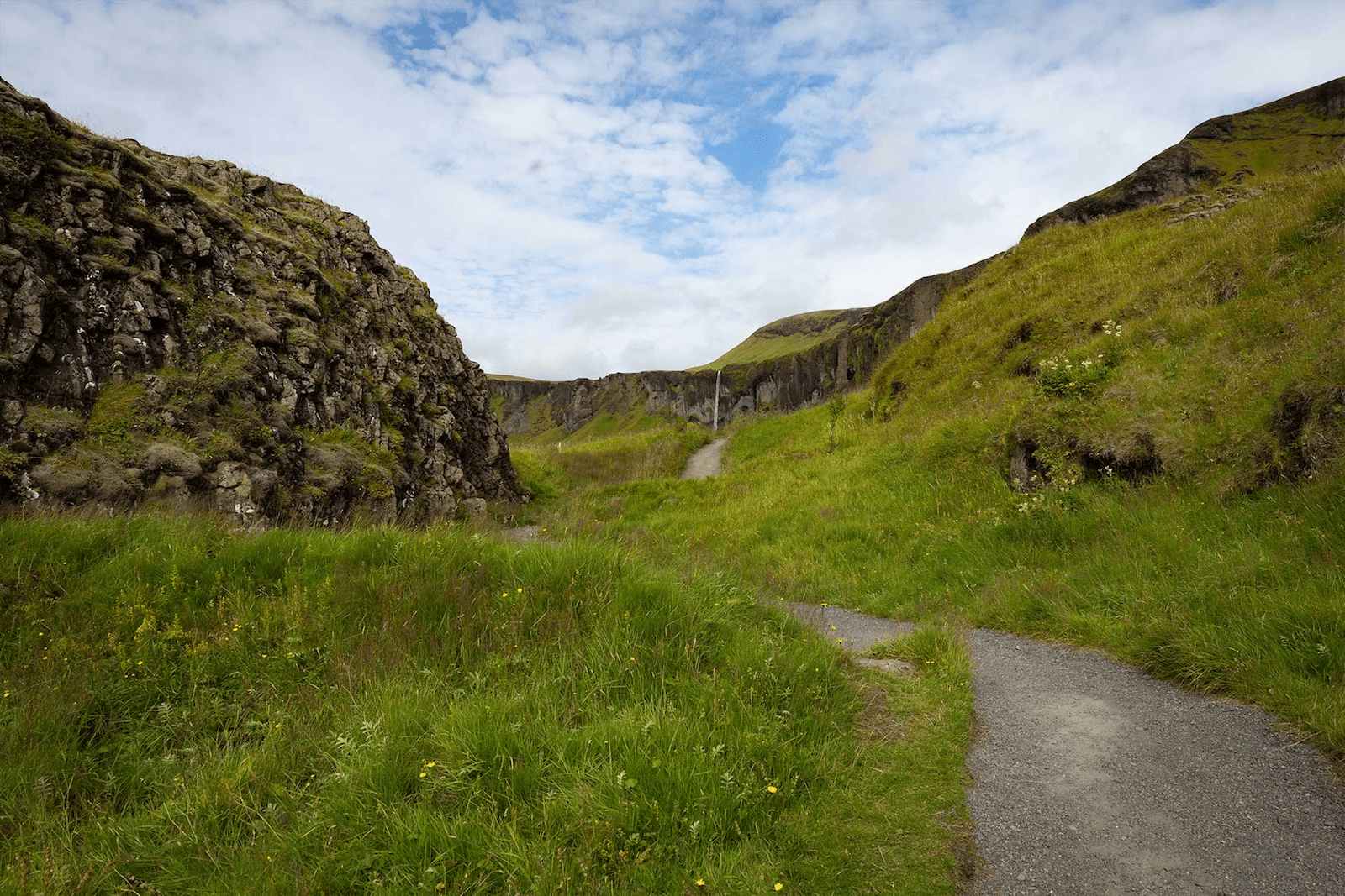 A path between grassy slopes and basalt outcrops at Dverghamrar, with Foss á Síðu visible beyond.