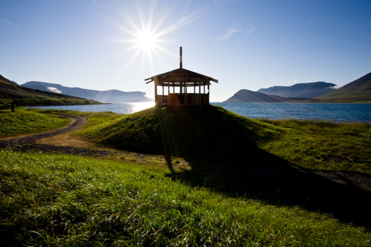 A small timber structure by the shore of Dýrafjörður near Þingeyri with mountains beyond.
