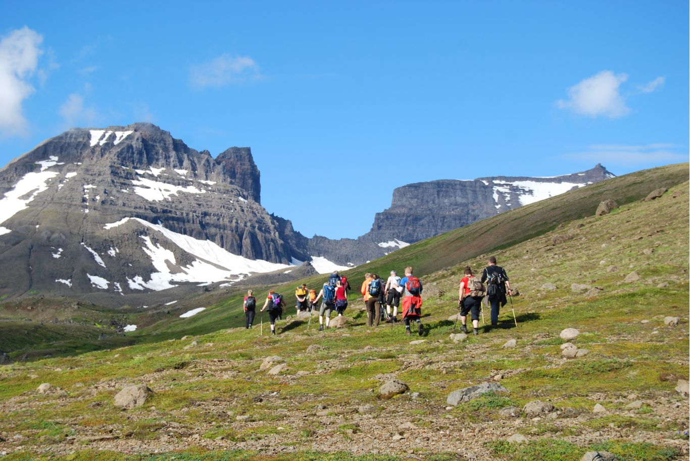 Hikers walking below the cliffs and snow patches of Dyrfjöll in East Iceland.