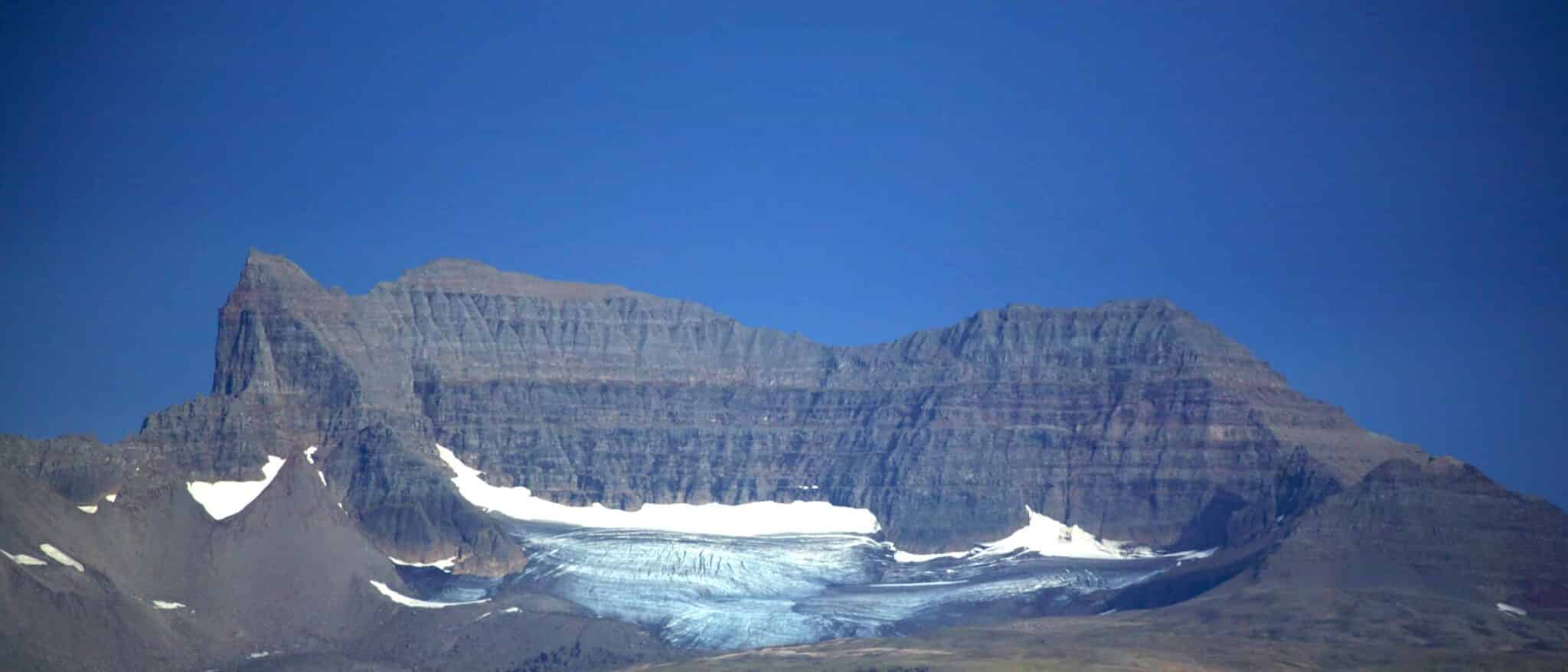 A broad view of Dyrfjöll with a snow-filled hollow beneath the dark mountain wall.