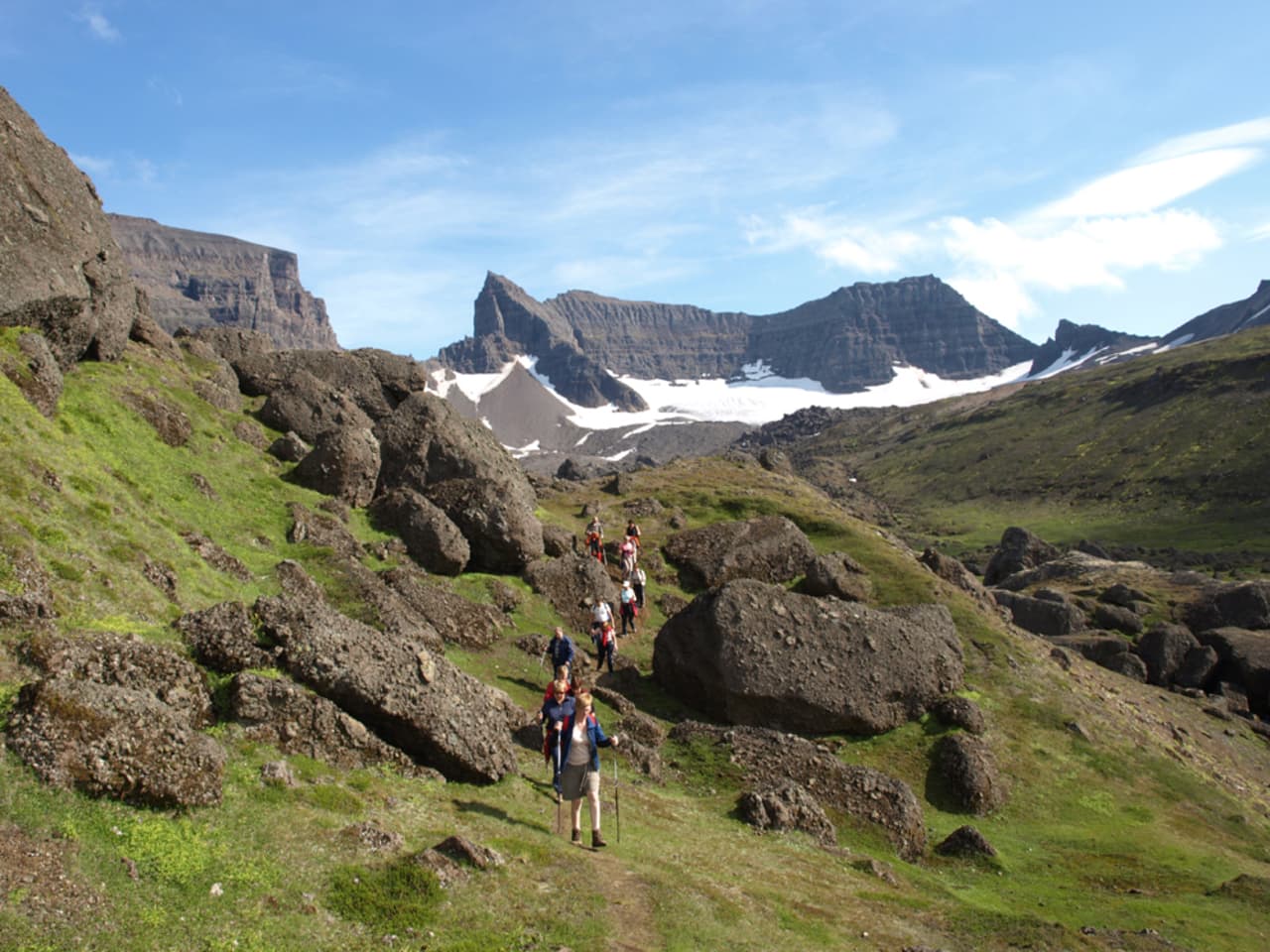 Hikers walking among boulders below the jagged Dyrfjöll mountain range in East Iceland.