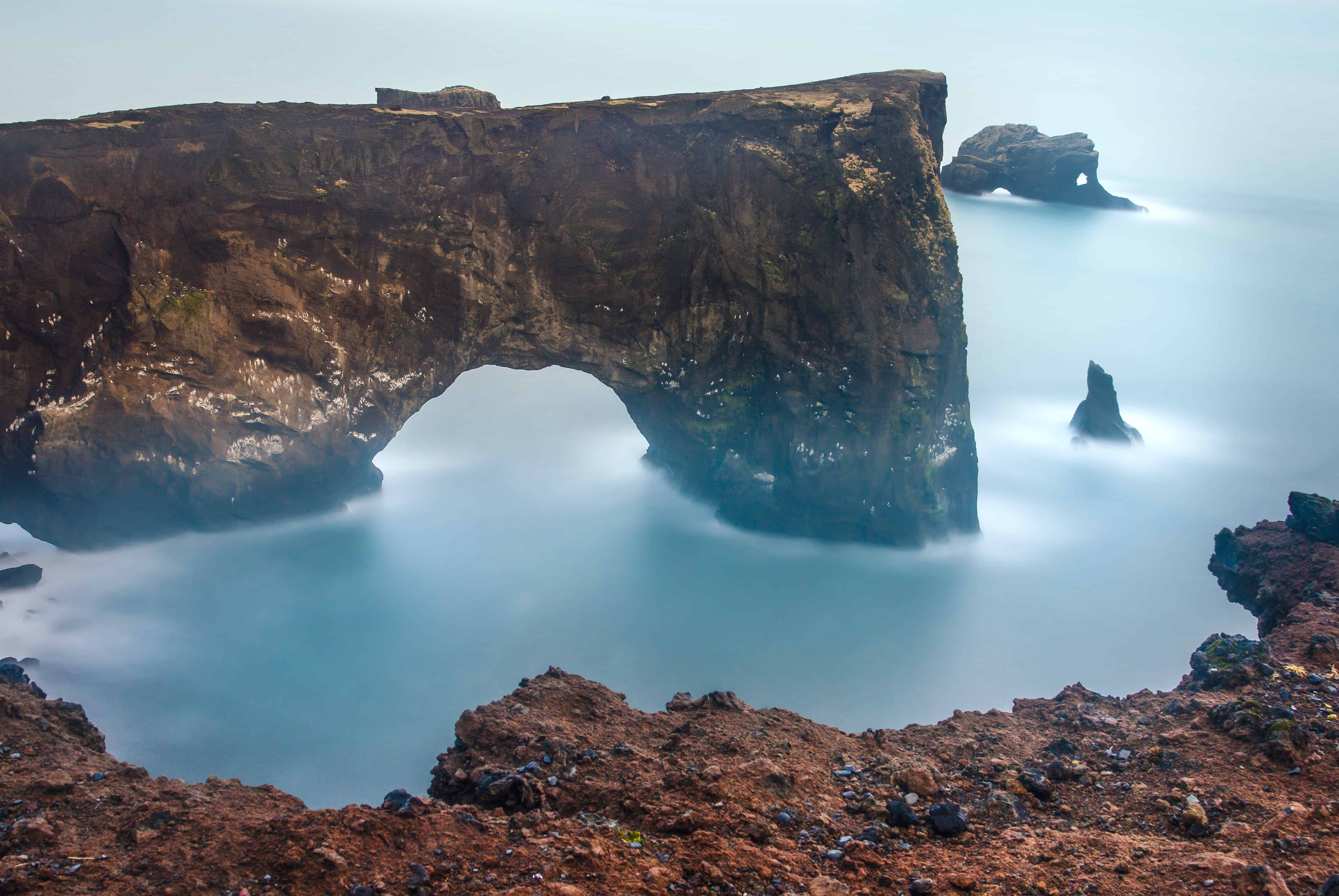 Dyrhólaey sea arch rising from the ocean with sea stacks beyond it.