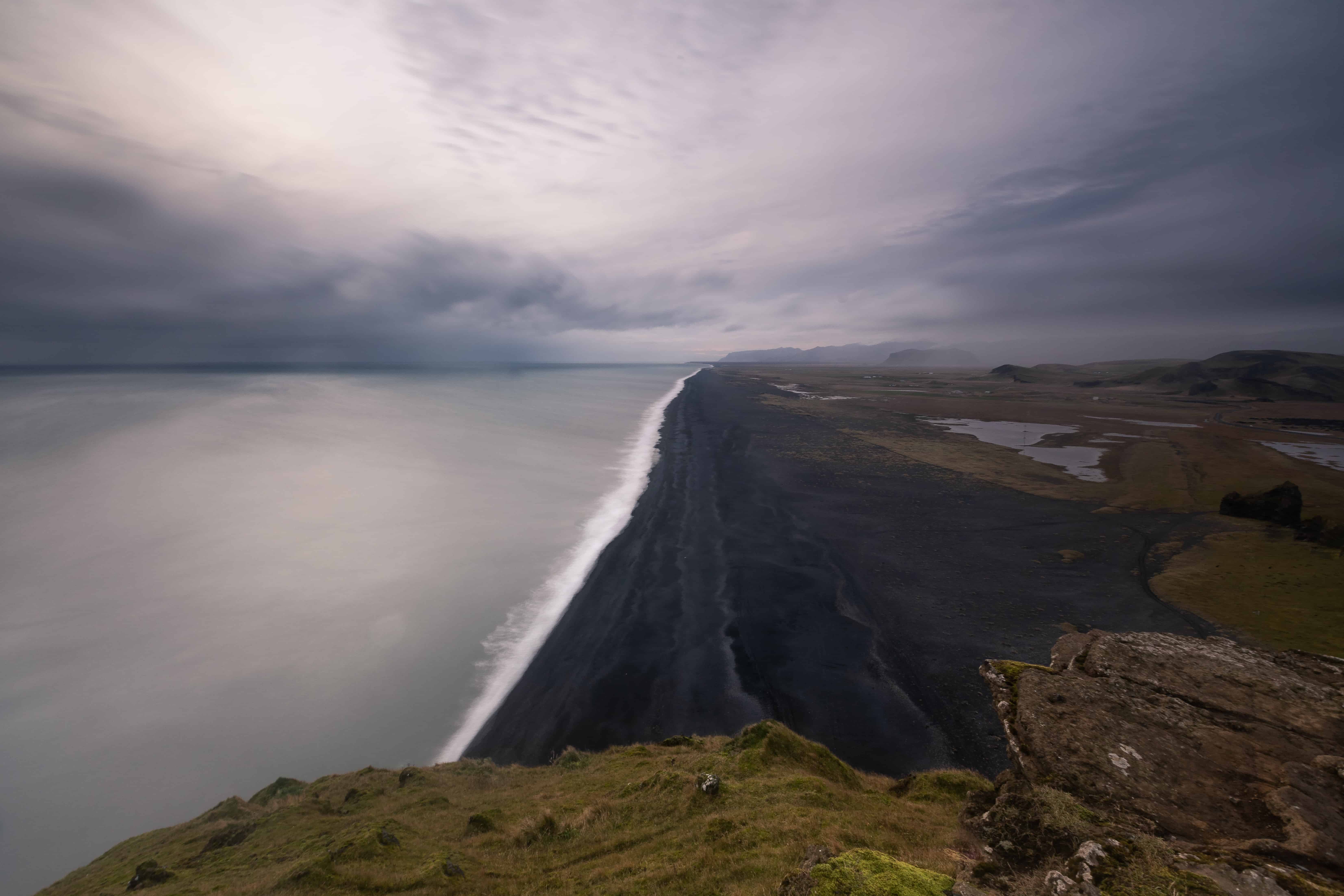 View from Dyrhólaey over a long black-sand beach and South Iceland coastline.